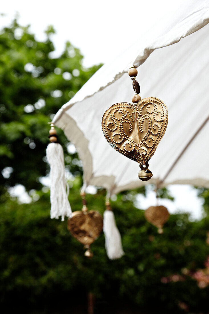Goldmetallic-Herzen hängen an einem Sonnenschirm im Garten in Brighton, East Sussex, England, UK
