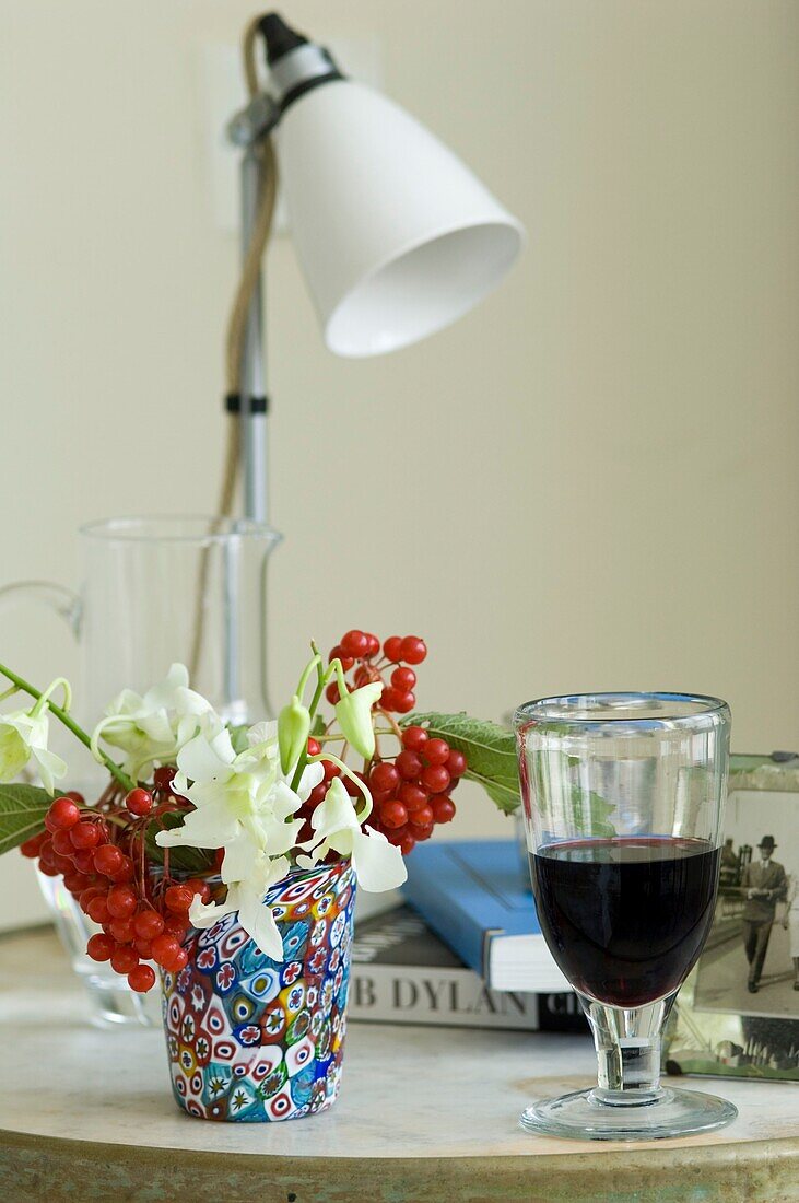 Stillleben mit Rotweinglas und kleinem Blumenarrangement in mehrfarbiger Vase