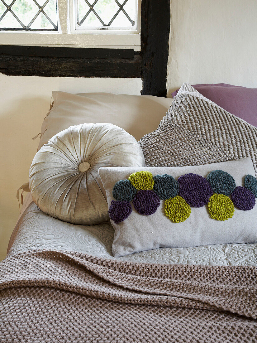 Variety of cushions on bed with blanket in Herefordshire cottage, England, UK