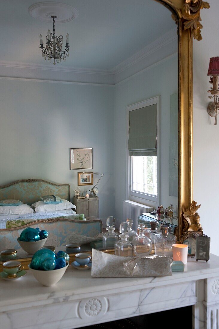 Marmorkamin mit großem vergoldetem Spiegel, in dem sich das Schlafzimmer mit verziertem, seidengepolstertem Bett spiegelt