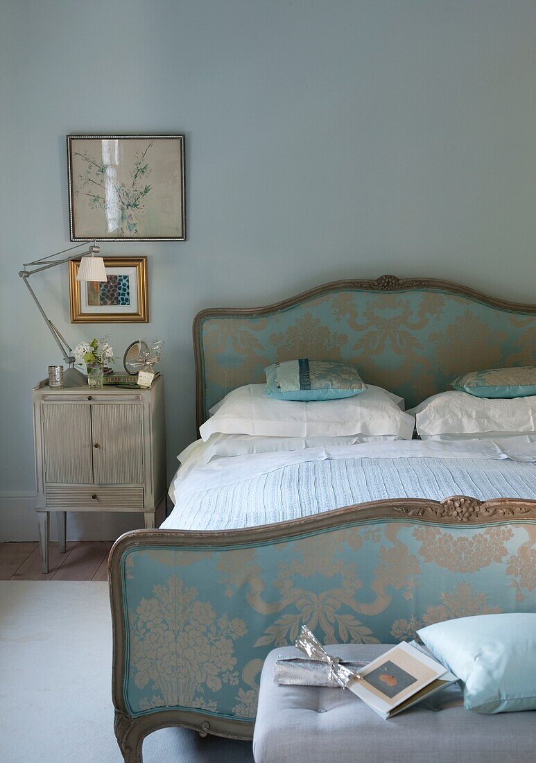 Gepolstertes Seidenbett in einem hellblauen Schlafzimmer mit Nachttisch und Gelenklampe