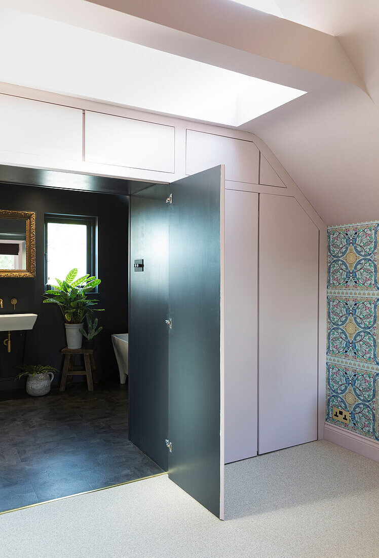 Die kontrastierenden, dramatisch dunklen Wände des En-Suite-Badezimmers verbergen sich hinter blassrosa Einbauschränken