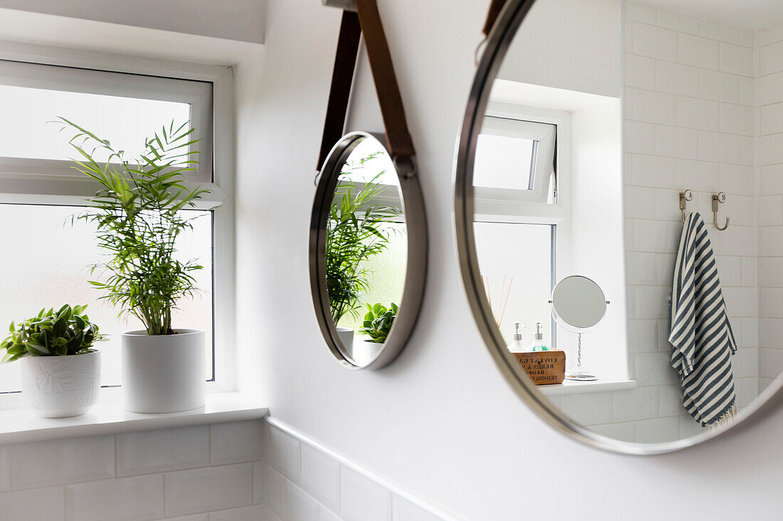 Zwei Spiegel hängen neben Zimmerpflanzen auf der Fensterbank und reflektieren das Badezimmer im Haus in Reigate, Surrey, UK