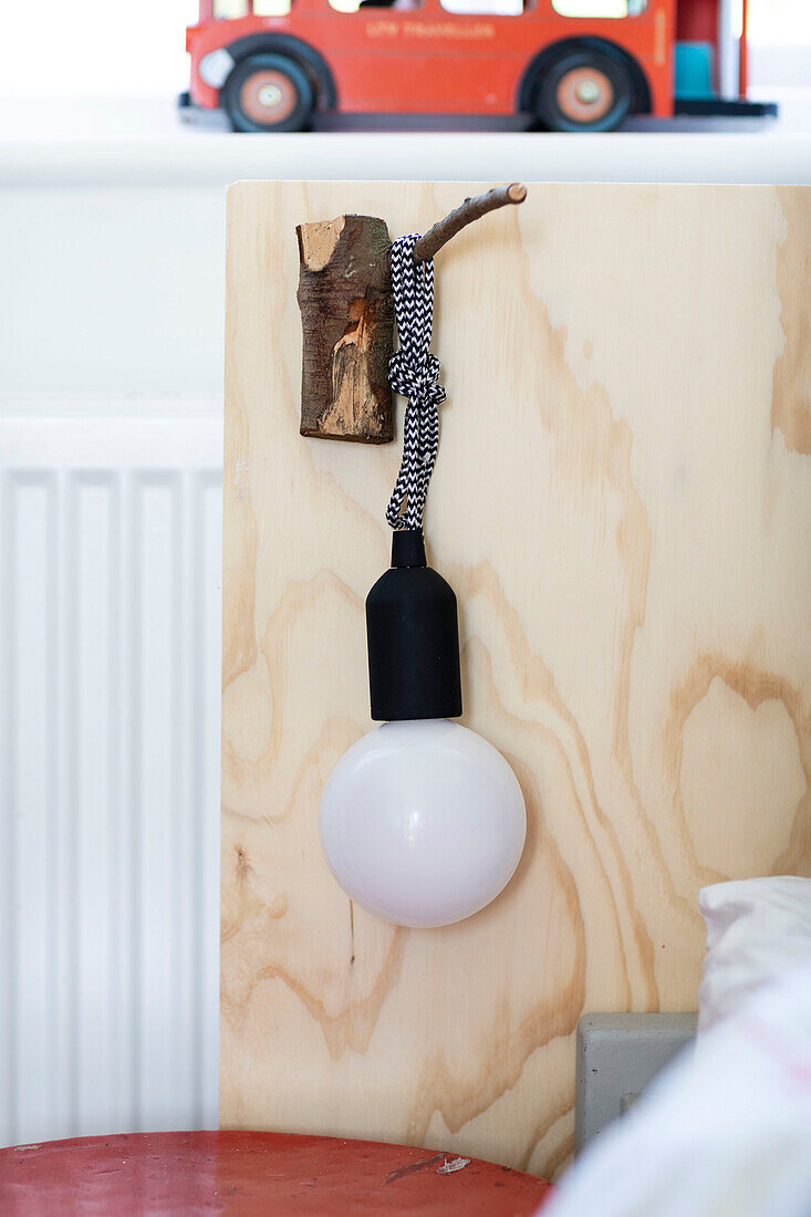 Bettkopfteil aus Sperrholz und Lampe an einem Holzhaken im Jungenzimmer in Colchester, Essex, UK
