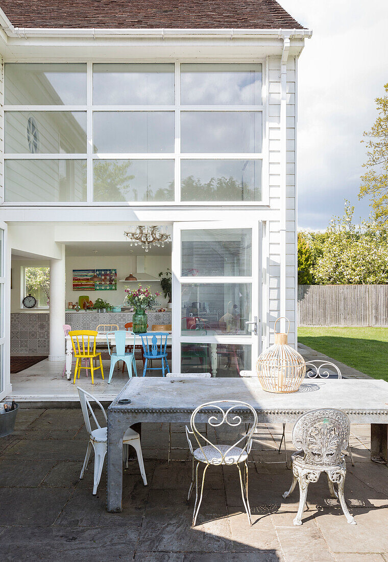 Sonnenbeschienener Tisch und Stühle auf der Terrasse eines Anbaus mit doppelter Höhe in einem Haus in Guildford, Surrey, UK