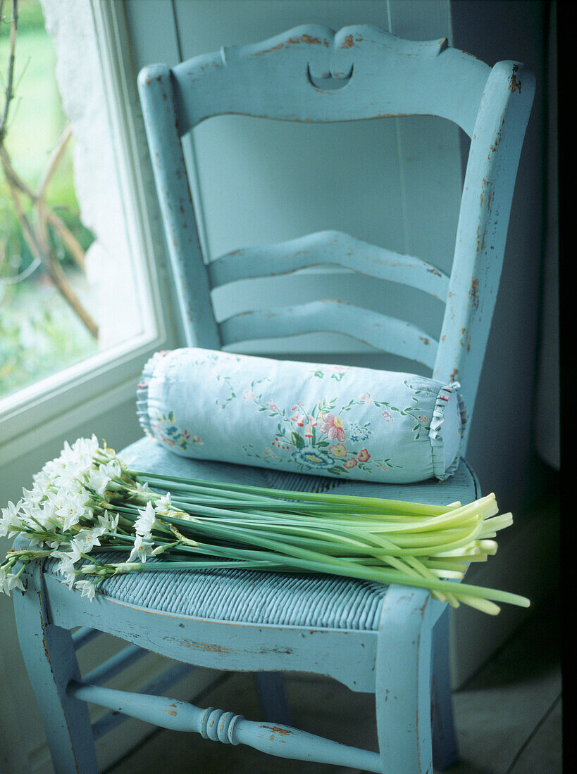 Hübscher blassblau gestrichener Stuhl mit Schnittblumen vor einem Fenster