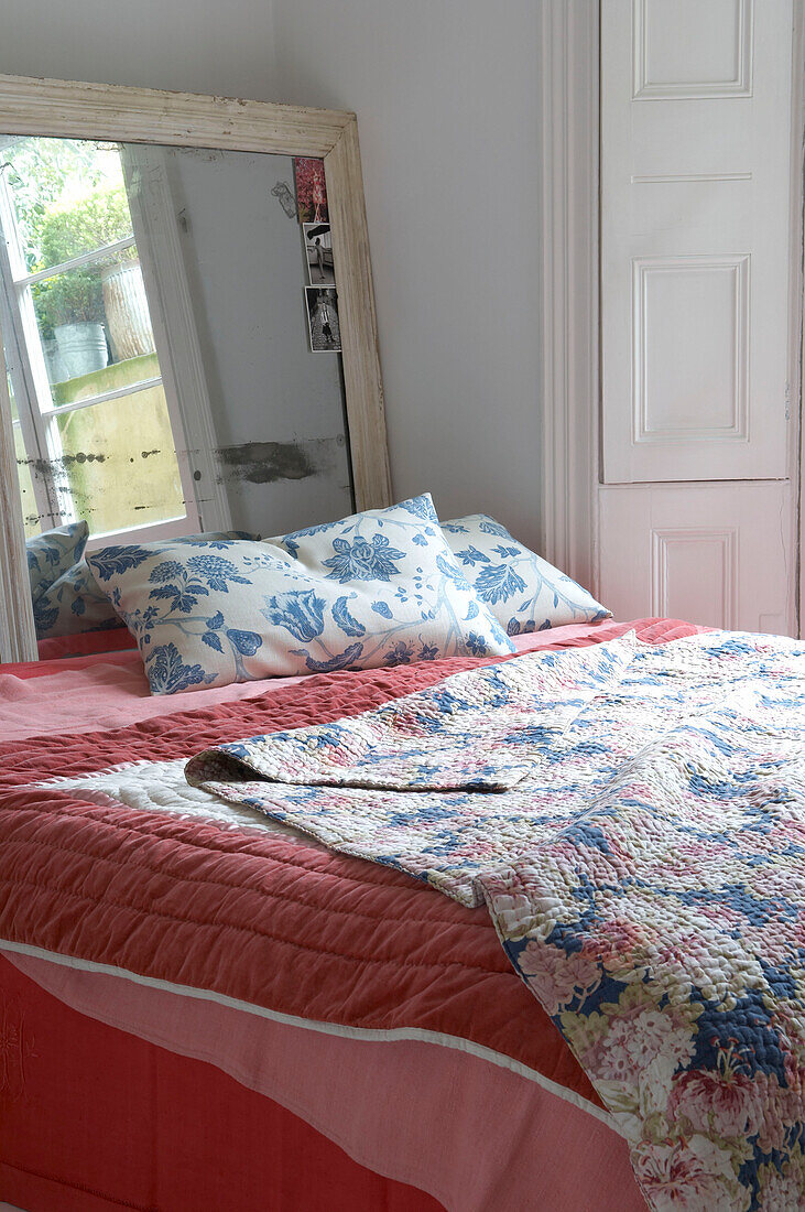 mit Blumen bedeckte Tagesdecken und Steppdecken auf einem Doppelbett mit großem Spiegel dahinter