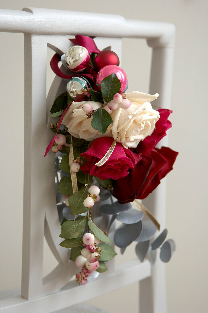 Weihnachtsblumenkranz mit Beeren und Kugeln an der Rückenlehne eines weißen Esszimmerstuhls
