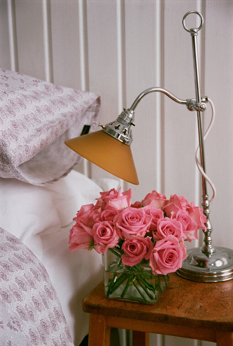 Detail von Nachttisch und Hocker mit rosafarbenem Blumenarrangement und Leselicht