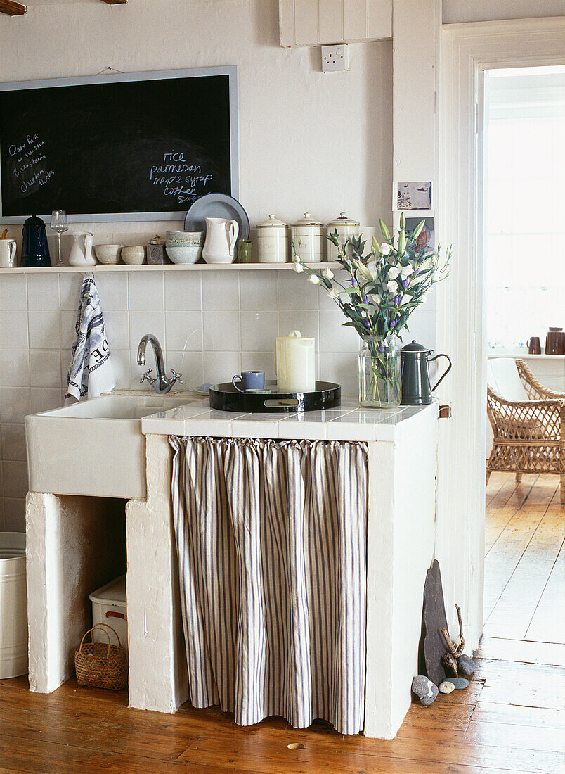 Küchenspüle im Butler-Stil in einem Betonschrank mit weiß gefliester Arbeitsplatte und gestreiftem Vorhang