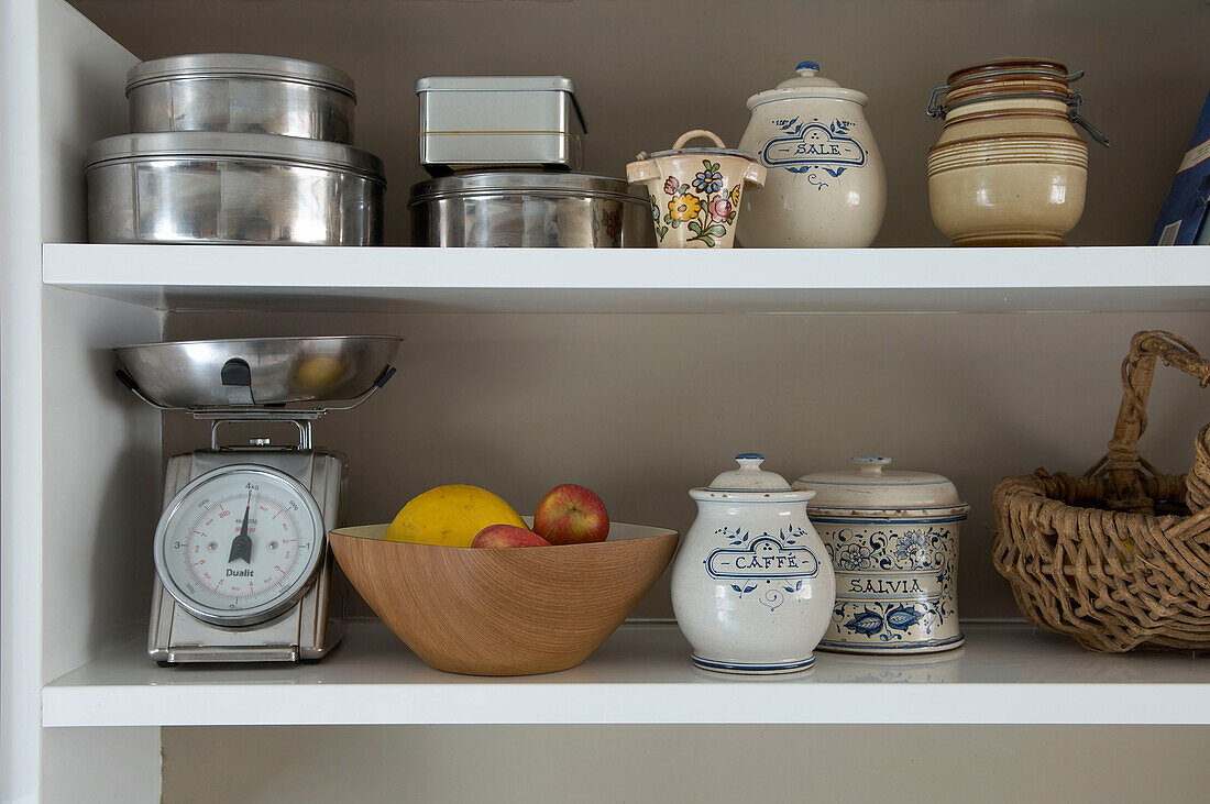 Baking tins and chinaware with weighing scales on kitchen shelves