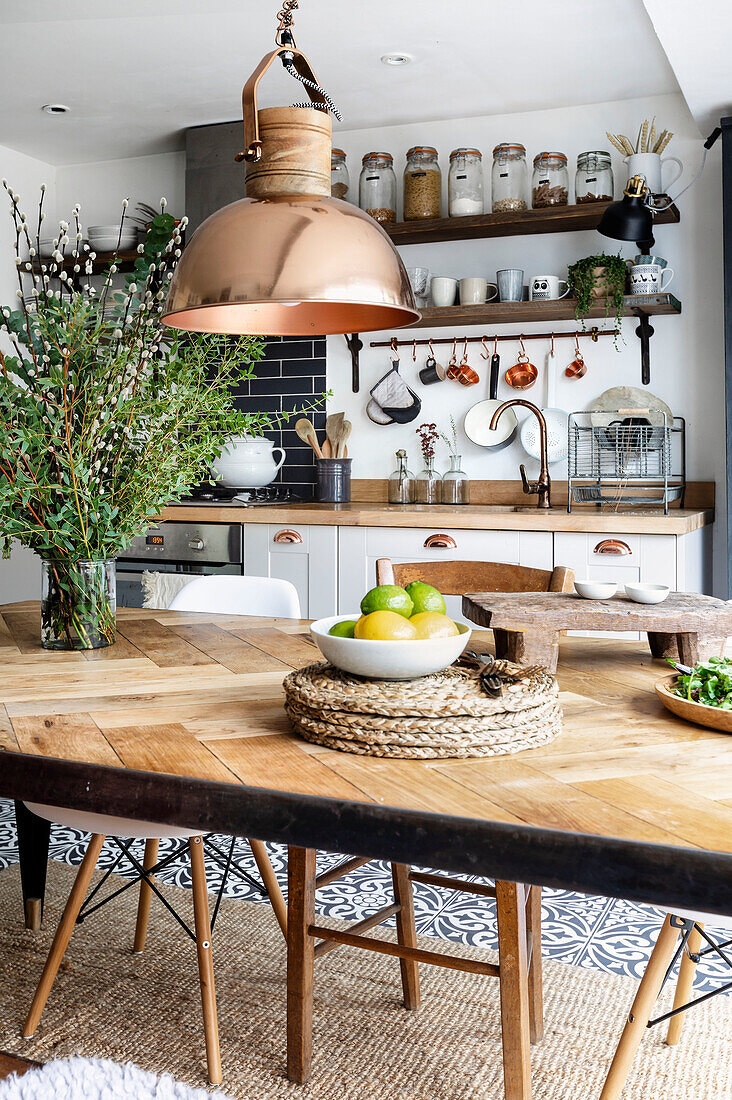 Kitchen table with large vase of foliage and industrial copper pendant light in Cardiff, Wales, UK