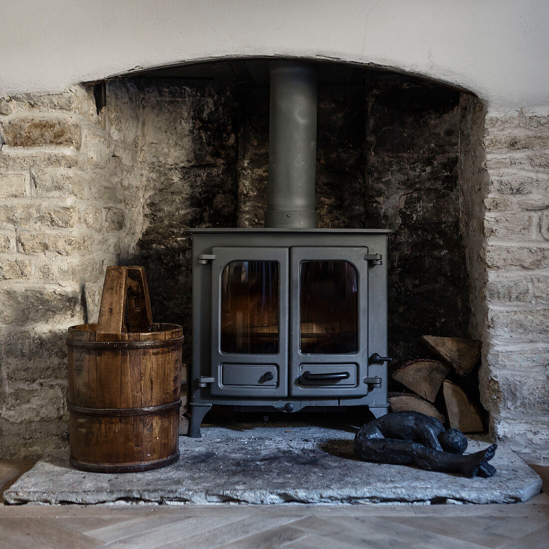 Holzofen mit antikem Eimer in offenem Steinkamin in einem Hause in Somerset, UK