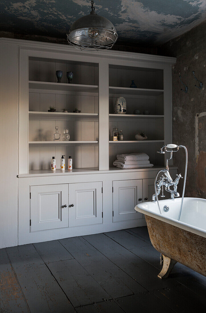 Großer Aufbewahrungsschrank und freistehende Badewanne mit industrieller Hängeleuchte in einem Haus in Somerset, Großbritannien