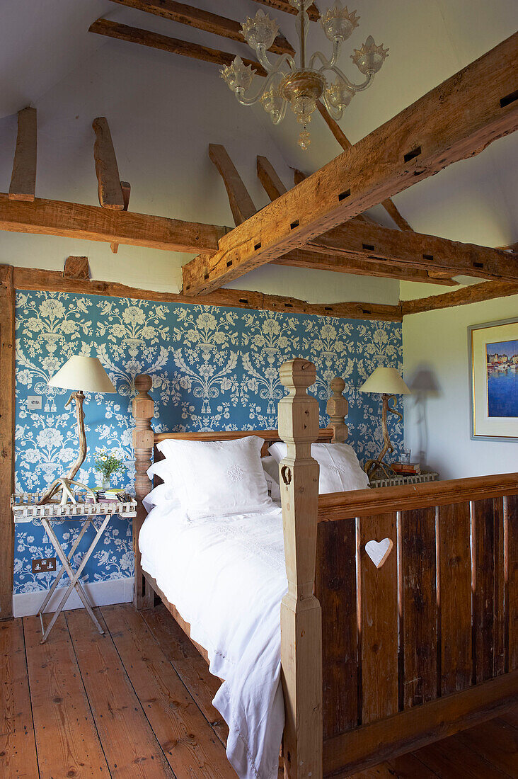 In das hölzerne Fußteil des Bettes geschnitztes Herz in einem blauen Zimmer mit Holzrahmen in einem Bauernhaus in Iden, Rye, East Sussex, Vereinigtes Königreich