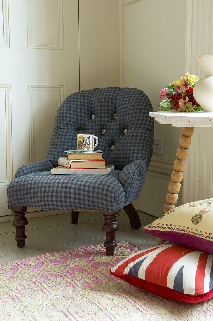 Bücherstapel und Tasse auf blauem Stuhl mit Knöpfen im Wohnzimmer eines Hauses in Suffolk, England, UK