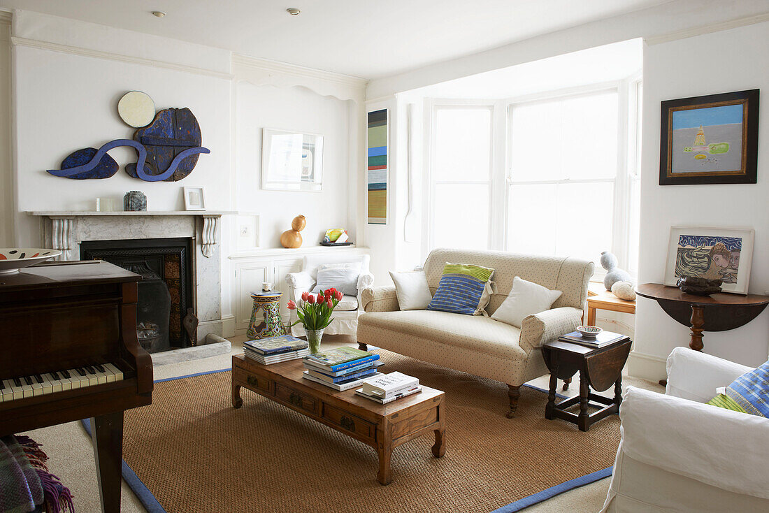 Klavier im Wohnzimmer mit Zweisitzer-Sofa und niedrigem Couchtisch aus Holz mit Büchern Aldeburgh, Suffolk England UK