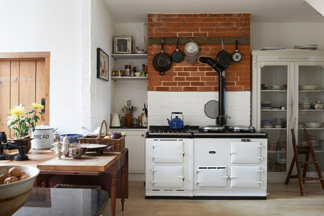 Kitchenware hangs on exposed brick wall above whitewashed range oven in Aldeburgh kitchen Suffolk England UK