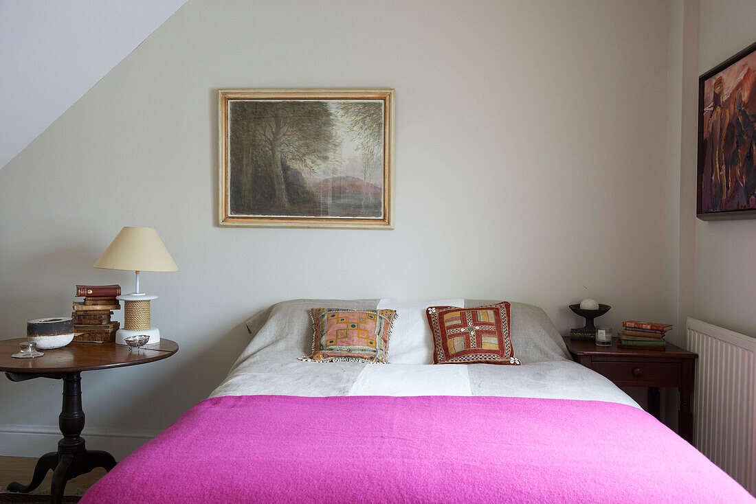 Framed artwork above double bed with bright pink blanket in Aldeburgh home Suffolk England UK