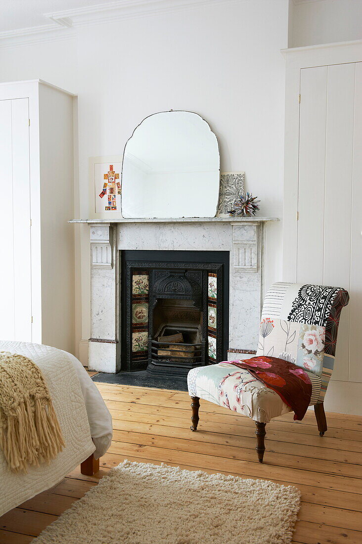Upholstered chair next to Victorian fireplace in bedroom of Broadstairs home, Kent, England, UK