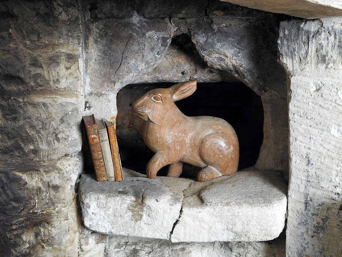 Hölzernes Kaninchen und drei Bücher auf Steinregal