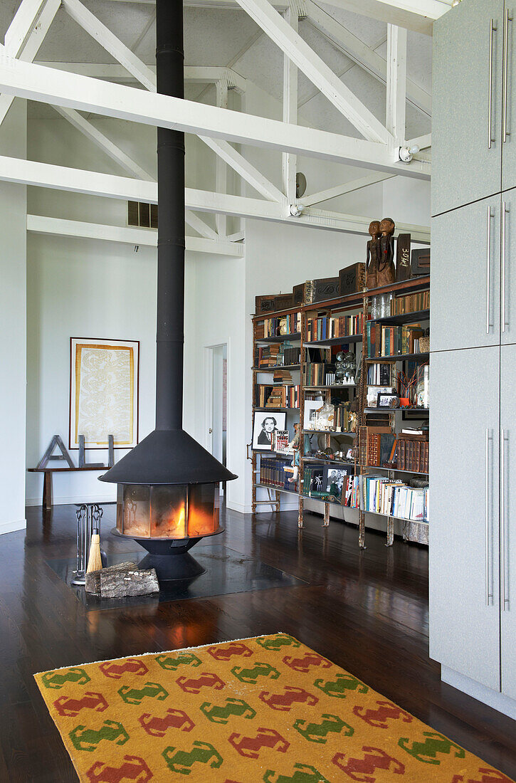 Freestanding lit fire and bookcase with patterned rug in Sheffield home, Berkshire County, Massachusetts, United States