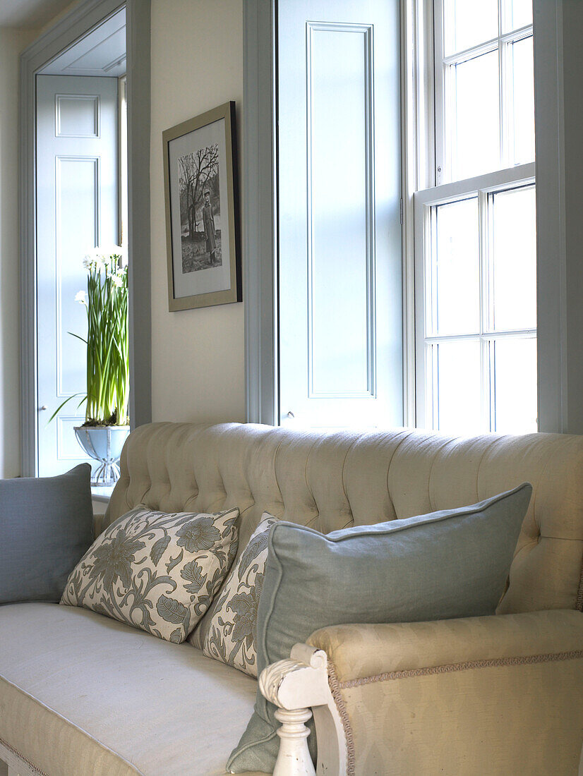 Gepolstertes Sofa mit Blumenkissen am Fenster eines Bauernhauses in Gloucestershire, England