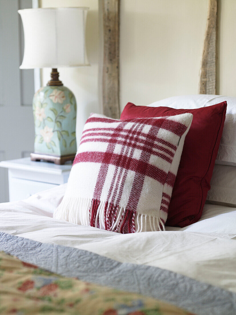 Red tartan cushion on bed in Gloucestershire farmhouse, England, UK