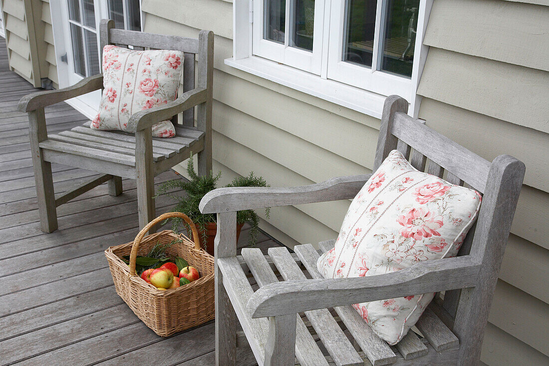 Passende Stühle mit Blumenkissen und einem Korb mit Äpfeln auf dem Balkon eines Bauernhauses in Hampshire, England, UK