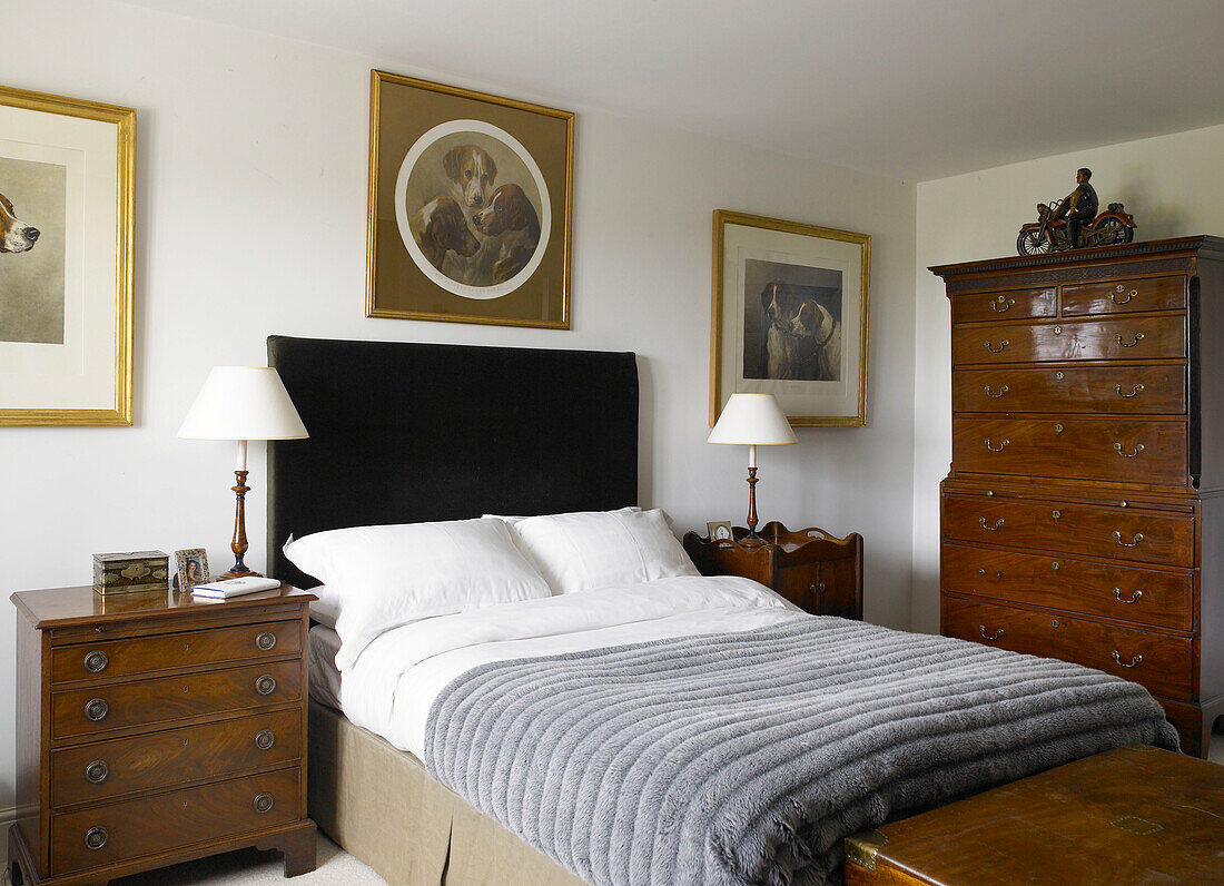 Pelzüberwurf auf dem Bett in einem Zimmer mit Tierporträts und einem hölzernen Tallboy in einem Bauernhaus in Hampshire, England, UK