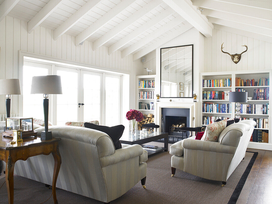 Bookcase and seating area in sunlit living room conversion of Hampshire farmhouse, England, UK