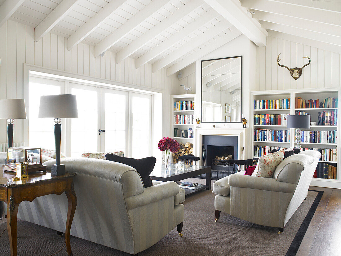 Bücherregal und Sitzecke im sonnendurchfluteten Wohnzimmer eines umgebauten Bauernhauses in Hampshire, England, UK