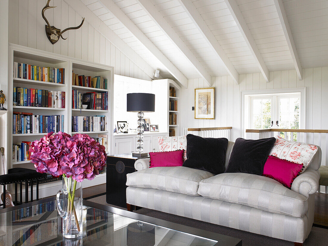 Bookcase and sofa with pink cushions in living room conversion of Hampshire farmhouse, England, UK