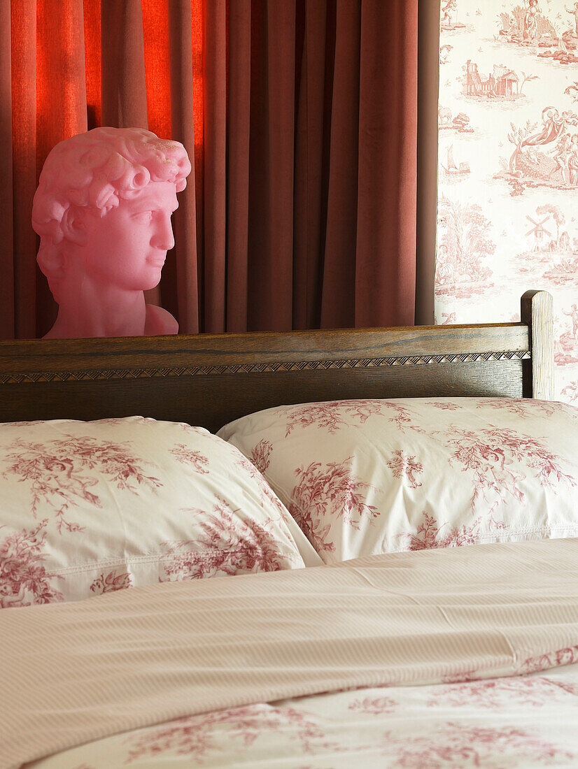 Pink bust and floral patterned pillows in bedroom detail of Welsh cottage, UK