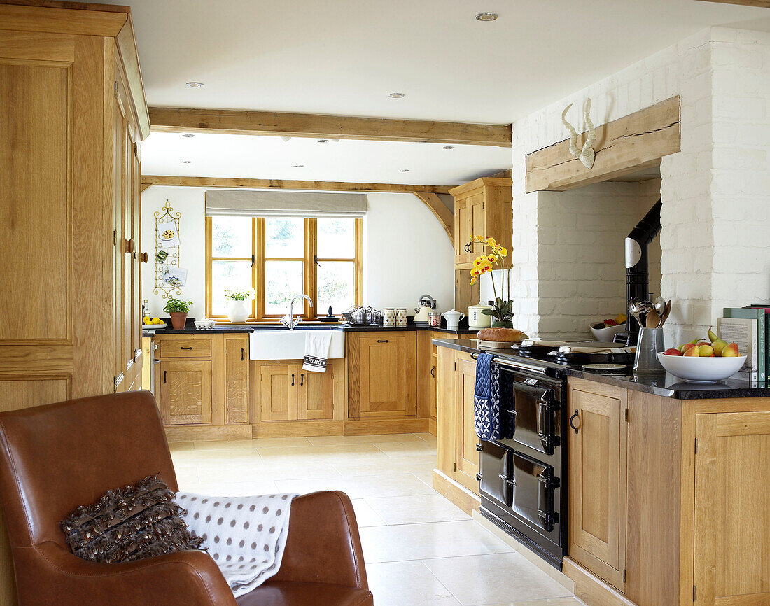 Brauner Ledersessel in offener Küche eines Landhauses in Gloucestershire, England, UK