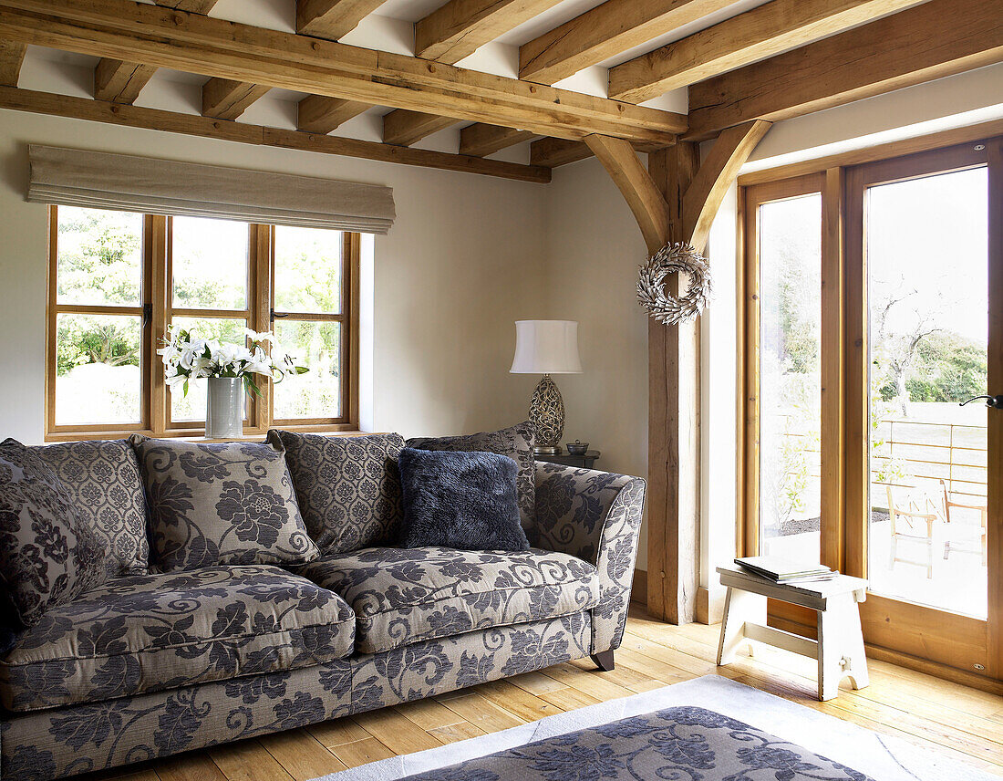 Floral gemustertes Sofa im Wohnzimmer mit Balken in einem Landhaus in Gloucestershire, England, UK