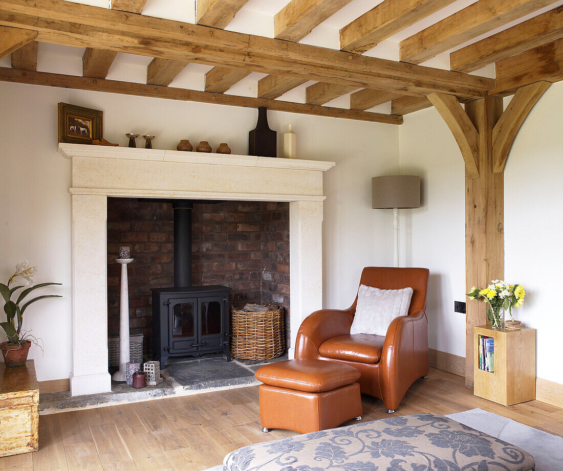 Matching leather armchair and footstool and recessed woodburner in fireplace of Gloucestershire cottage England UK