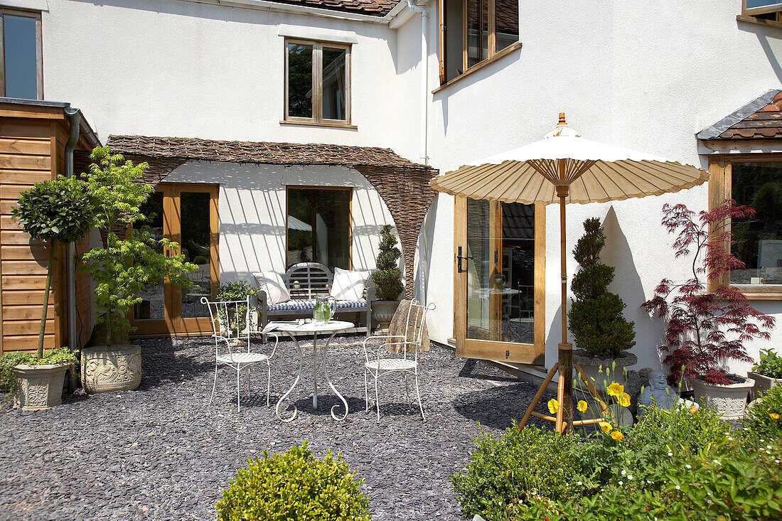 Tisch und Stühle mit Sonnenschirm im Garten eines Neubaus in Somerset, ländliches England, UK