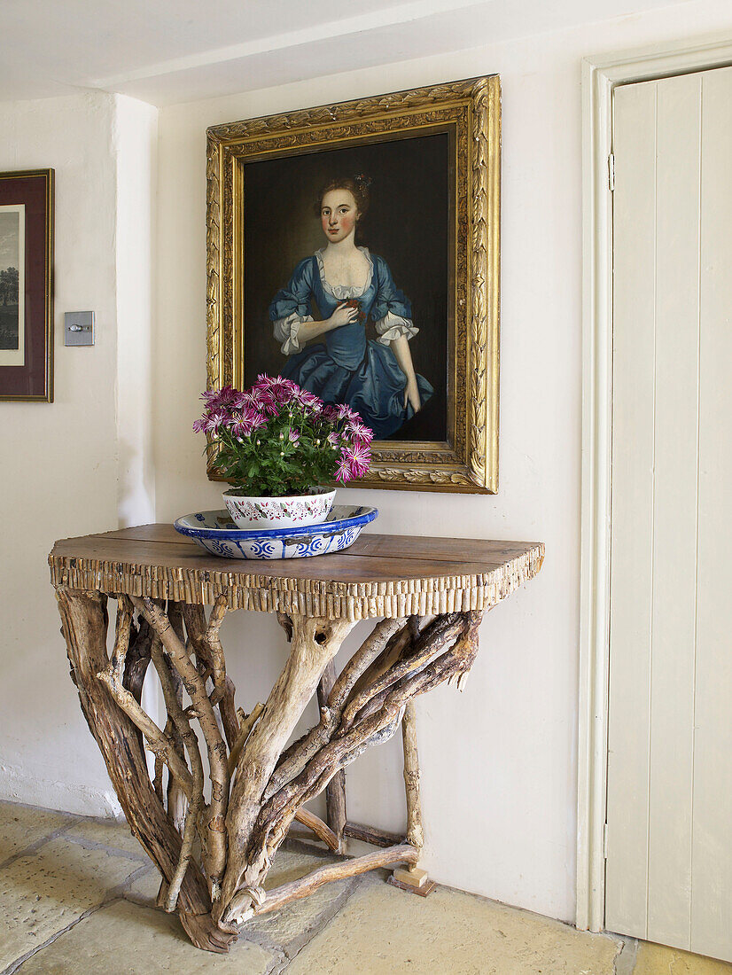 Driftwood side table and gilt framed oil painting in hallway of Gloucestershire home, England, UK