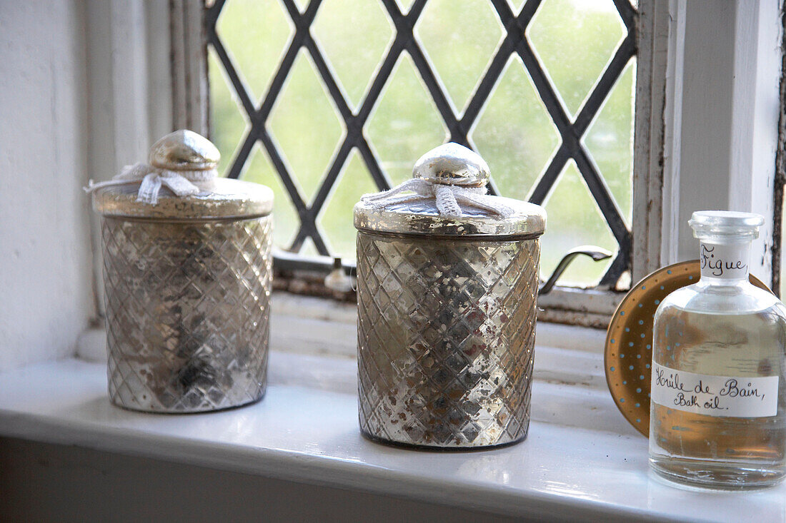 Silver storage jars and medicine bottle beside leaded window in country house Suffolk, England, UK