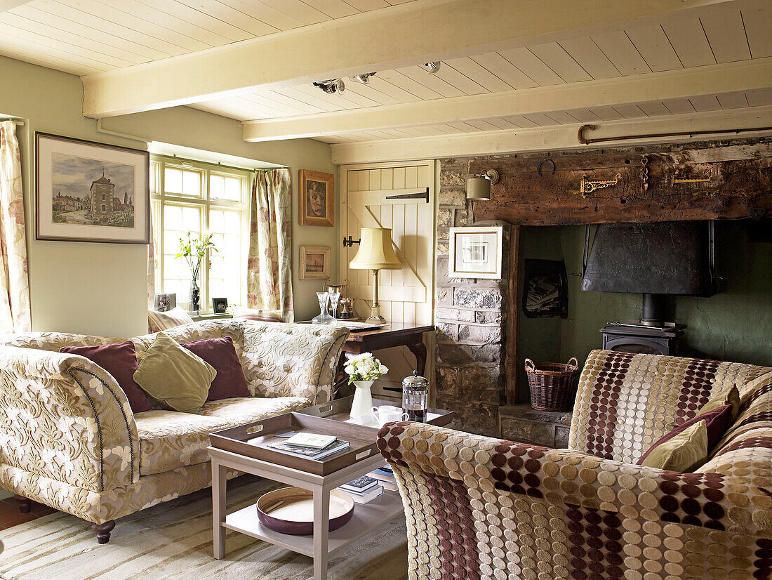 Mit strukturiertem Stoff gepolsterte Sofas und Holzofen im Wohnzimmer eines walisischen Cottage, UK
