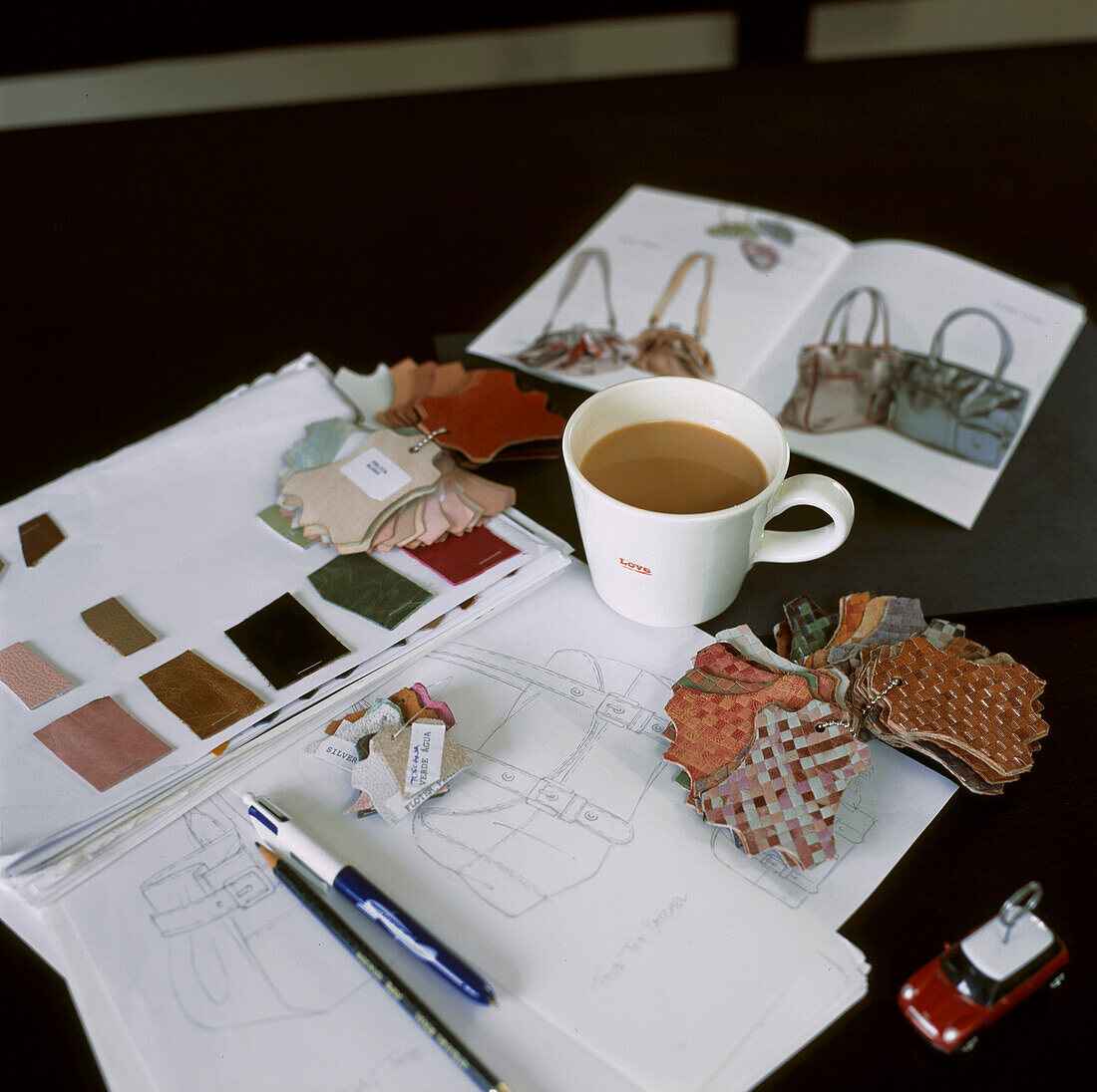 Skizzen, Arbeitsmappen, Muster und eine Tasse Tee auf dem Schreibtisch im Heimbüro