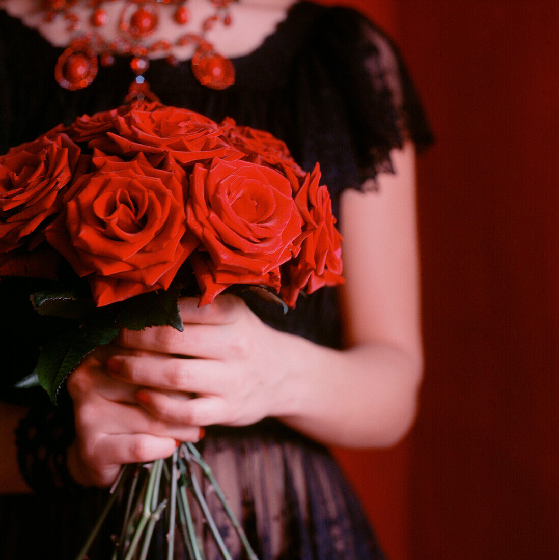 Frau im schwarzen Kleid hält einen Strauß roter Rosen