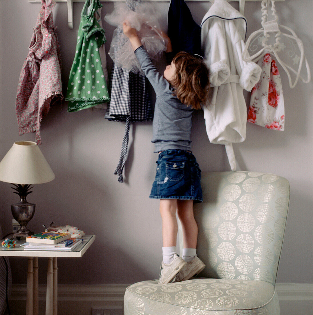 Child standing on a chair reaching for her dressing up clothes