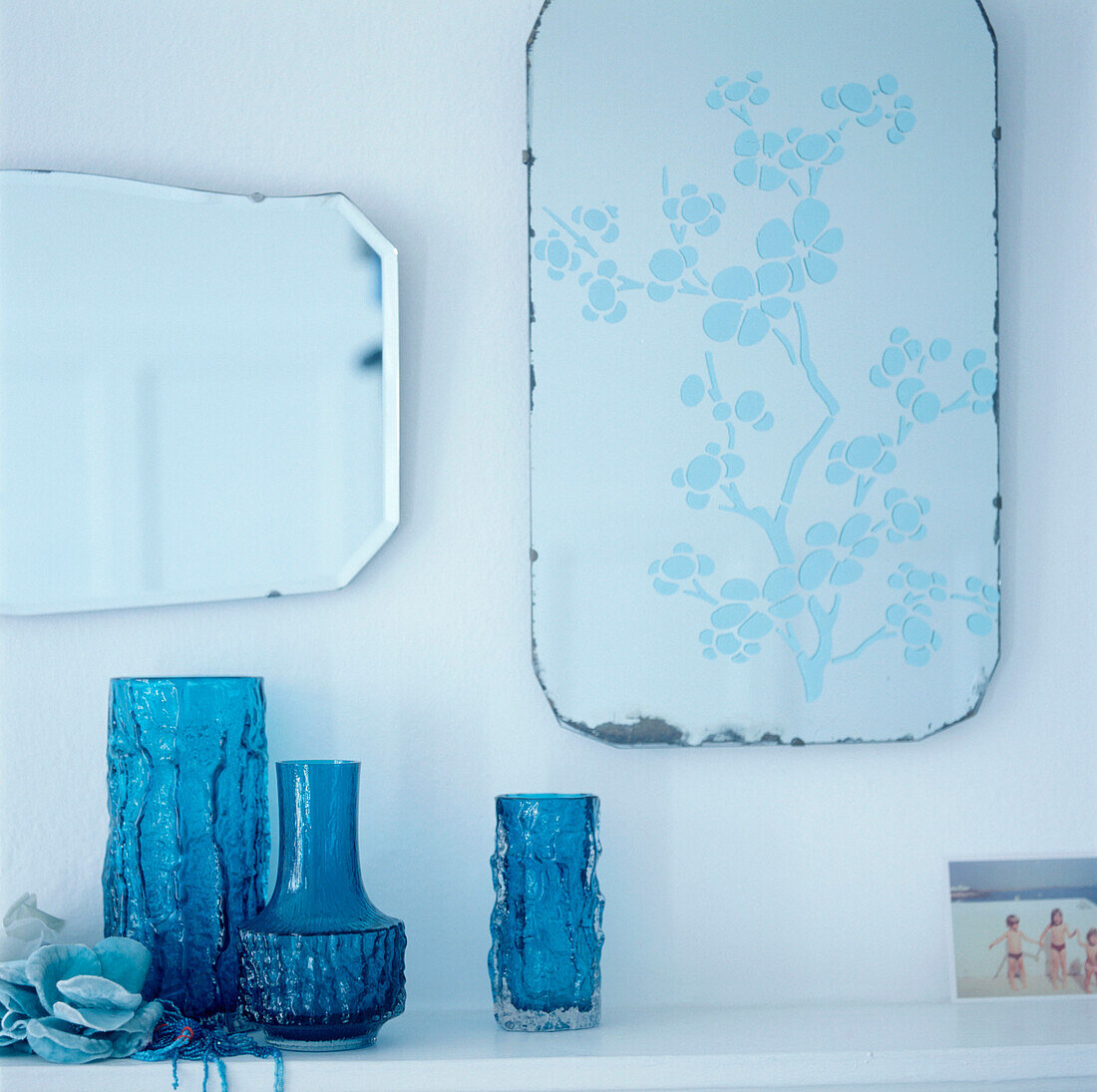 Detail von türkisblauen Glasvasen auf einem Regal mit Spiegeln an der Wand