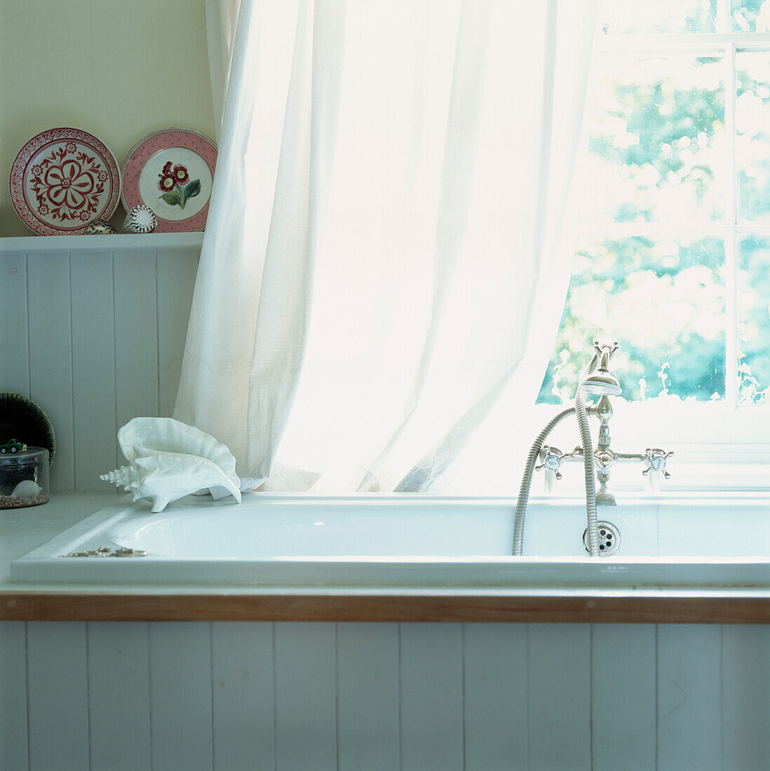 Große Badewanne mit alten Armaturen unter dem Fenster in weiß getäfeltem Bad