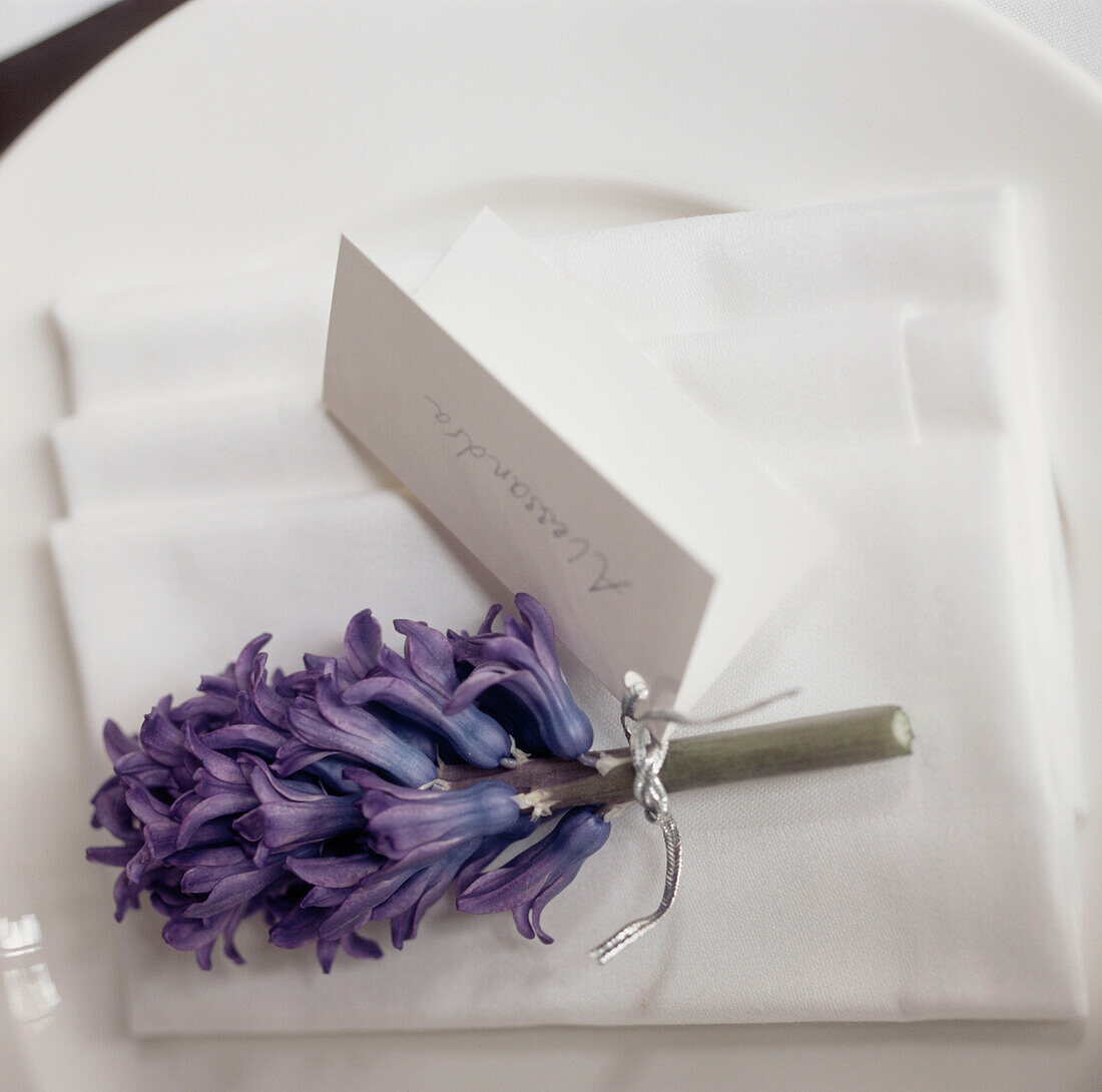 Detail of a white table setting with a name tag attached to a purple hyacinth