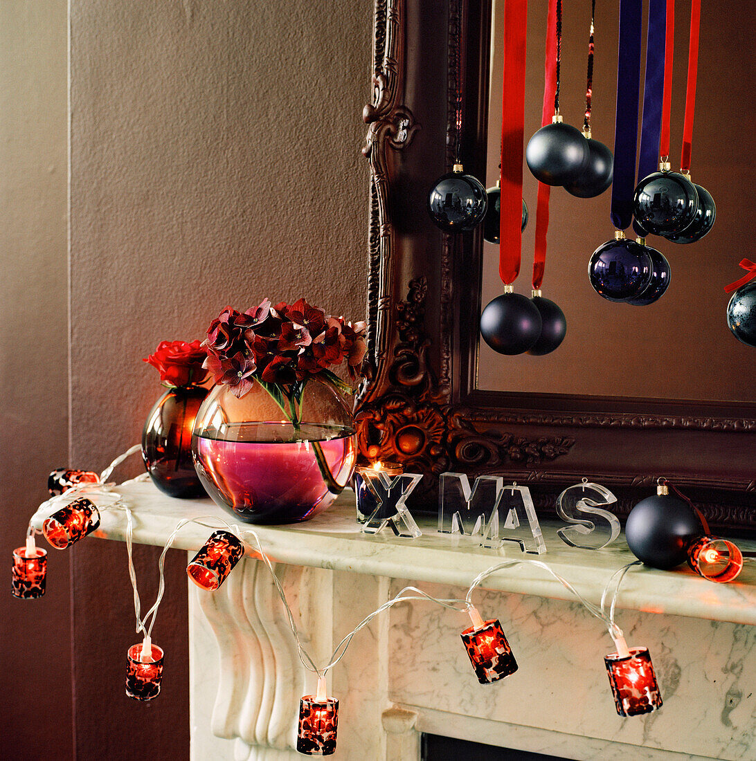 Mit Weihnachtsdekoration und Lichterketten geschmückter Kaminsims im Wohnzimmer