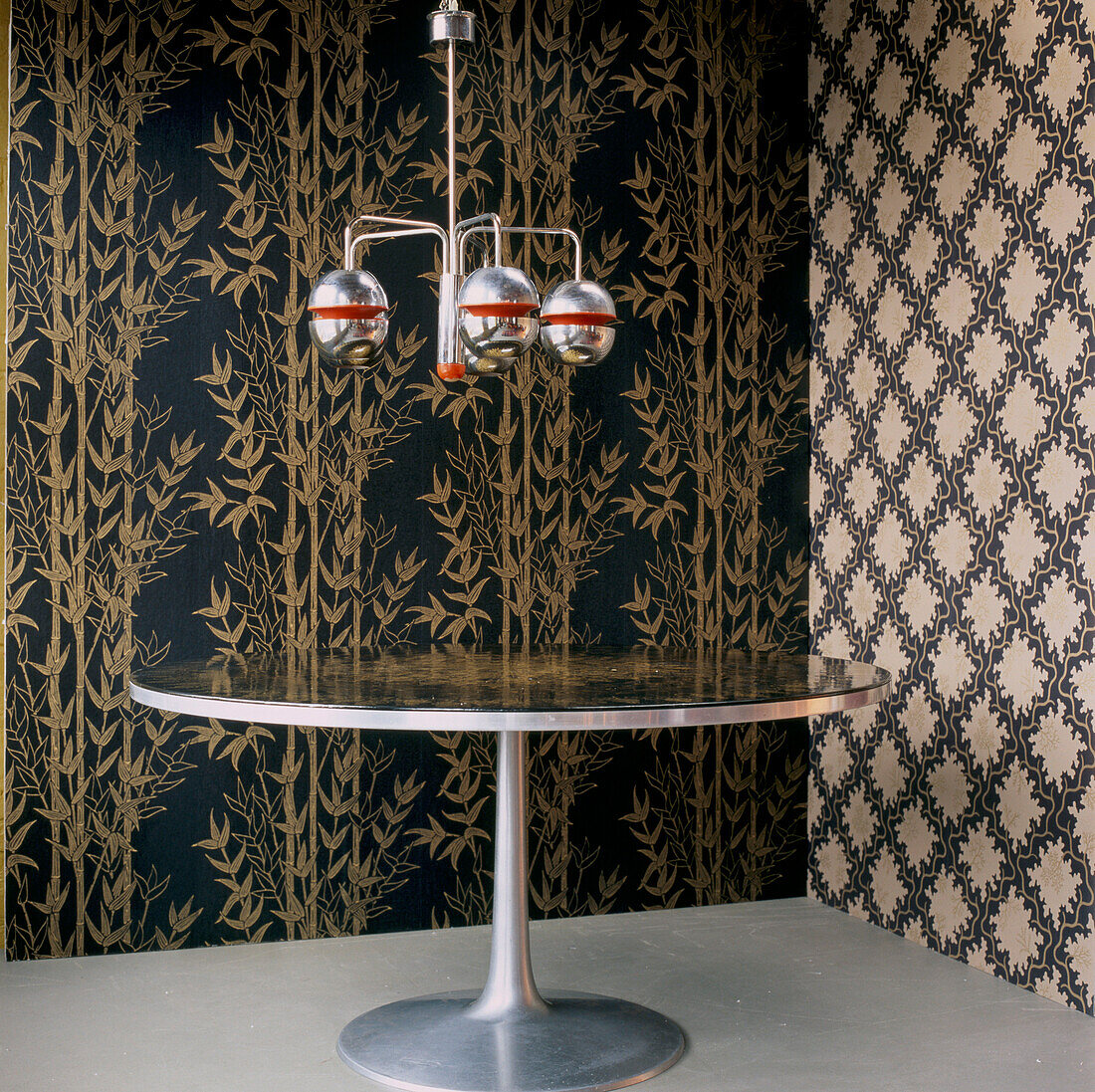 Heavily patterned wallpaper in a dining room with round metallic table and retro chandelier