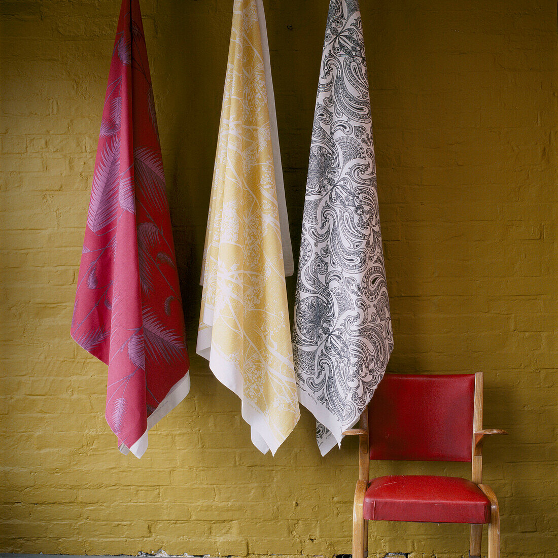 Fabric hanging on hooks against a painted brick wall and armchair 
